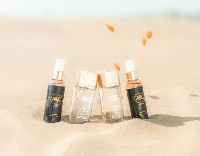 Four A&C perfume sprays standing in sand with dried grass