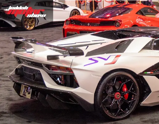 White supercar with a purple stripe next to a red sports car on the show floor